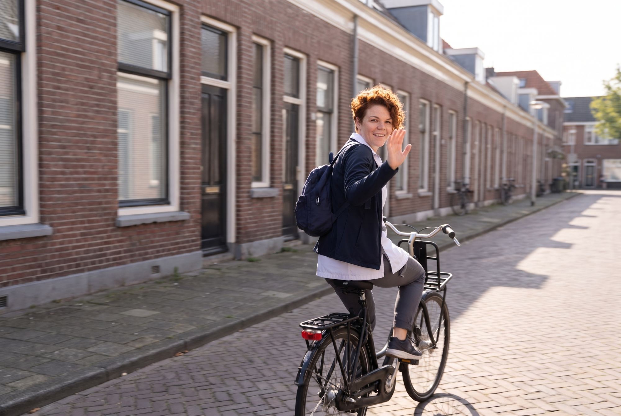 Zorgmedewerker fietst weg door een Haagse straat en zwaait over haar schouder